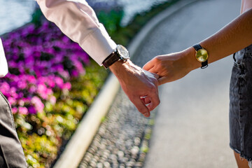 Closeup on couple in love. Happy lovers holding hands together with sunny outdoors. with watches on hands. flowers in background