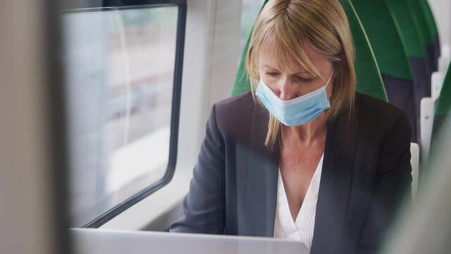 Mature businesswoman wearing face mask on train working on laptop - shot in slow motion