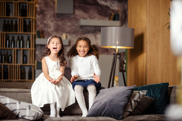 Obraz premium Two beautiful little girls are sitting on the back of sofa.