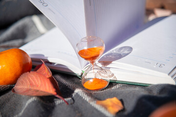 Hourglass on the background of a diary with autumn leaves. Concept of passing time