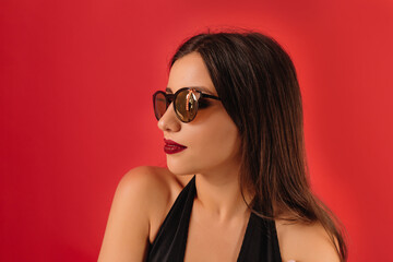 Indoor portrait in profile of charming caucasian woman with long hair in sunglasses over red background