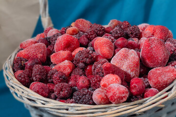 Selected focuse of Frozen berry in a wicker basket.  Mix: cherries, currants, blackberries, strawberries on a blue and beige textile background.