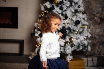 Fototapeta na wymiar Happy smiling mixed girl with dark hair sitting on the carpet. Christmas tree in the background.