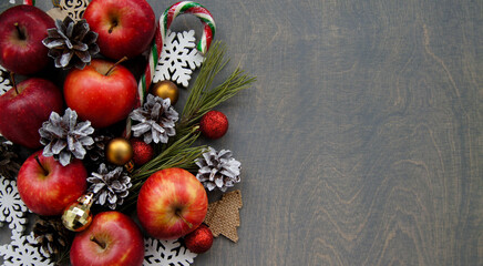 Obraz na płótnie Canvas Christmas background with pine branches, red apples and snowy cones. Dark wooden table.Top view. Space for text.