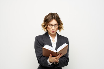 Woman at work with book in hand light background classic suit glasses head