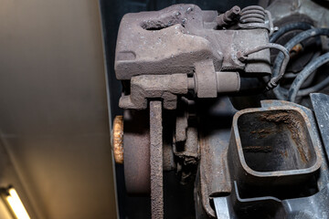 Old and damaged rear brake discs with caliper and brake pads in the car, on a car lift in a workshop.