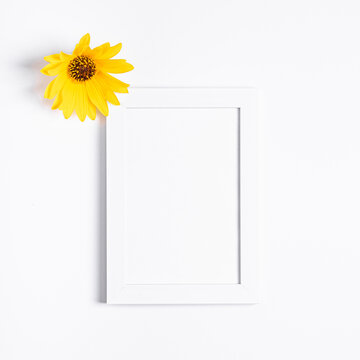 White empty picture frame mock up with yellow flower on white background, flat lay