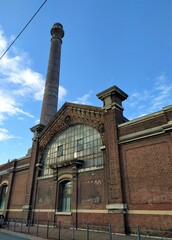 Fototapeta premium Patrimoine industriel - vieux bâtiment en briques rouges typique du Nord avec son entrée surmontée d'un fronton en verre et sa cheminée - Lille octobre 2020