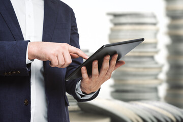 Businessman hand clicks on the screen of a digital tablet on the background of stacks of coins, close up. Online trading Concept