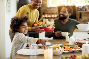 Happy black girl and her family setting the table for Thanksgiving lunch at home.