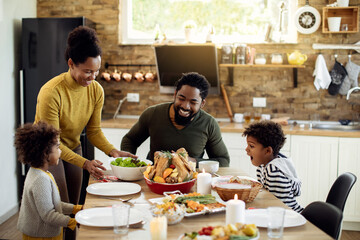Happy African American family enjoying in Thanksgiving lunch in dining room. - Powered by Adobe