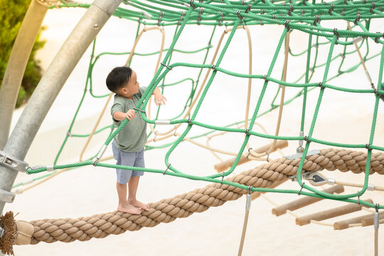 asia boy enjoying activity in a climbing adventure park on a summer day. Boy climbing ropes