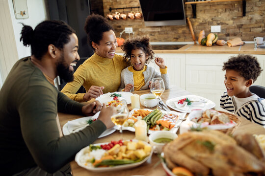 Cheerful black family having fun during Thanksgiving meal at dining table.