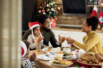 Happy black parents toasting with wine during family lunch on Christmas day.