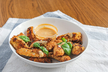 A bowl of chicken fingers and honey mustard sauce topped with basil leaves. Baked chicken slices served on the table as a starter of finger food. 