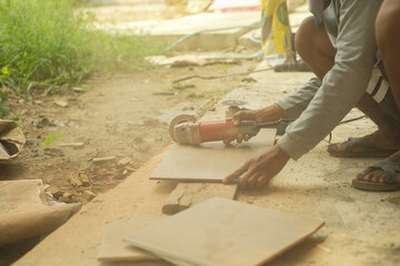 Workman cutting the floor tile by the electrical cutting machine at the construction site with cloud of dust in environment.