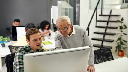 Aged man, senior worker training, mentoring, giving advice to new employee while standing in the...