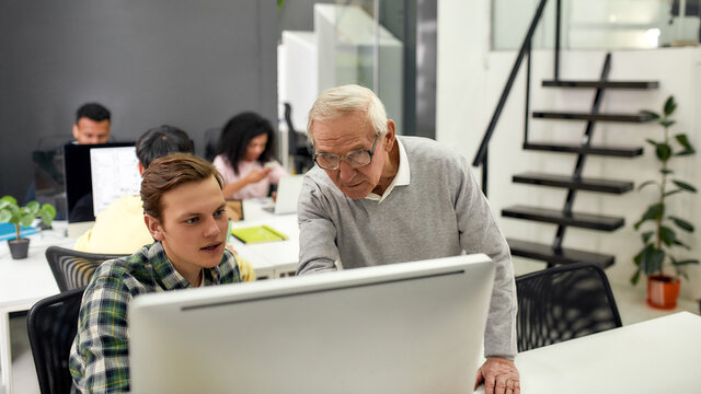 Aged man, senior worker training, mentoring, giving advice to new employee while standing in the office