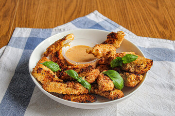 A plate of chicken fingers with honey mustard sauce. A crunchy chicken finger dipped into the sauce. Appetising and crunchy. 