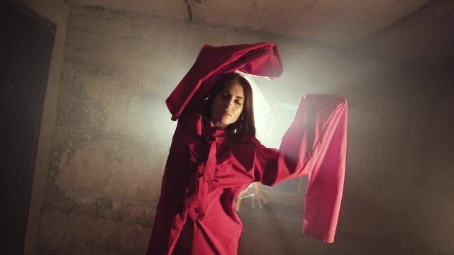 Silhouette of a mad girl in a red straitjacket. Bright rays of light in the dark