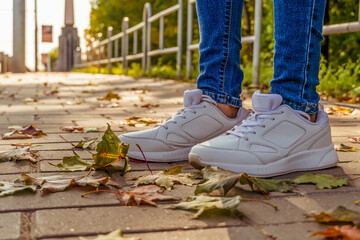 White sneakers on the sidewalk in autumn among the fallen yellow leaves on a Sunny day, copy space.