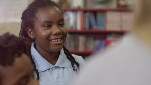 Young black student listens to teacher and smiles and laughs in classroom