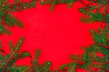 Christmas tree branches with red beads, snow, snowflakes with copy space in the center on a red background, top view. Greeting card for Christmas and new year. Beautiful Christmas background.