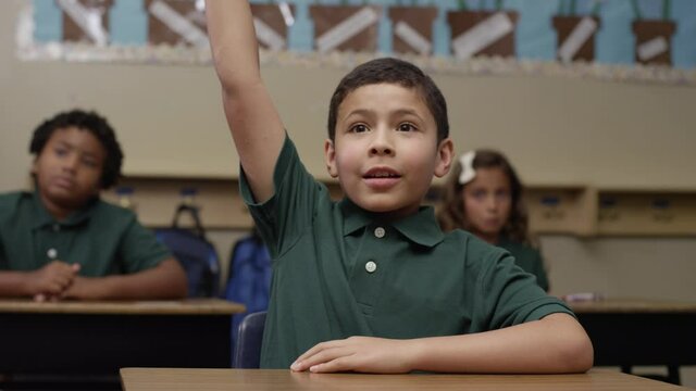 Primary Students In Uniforms Sit In Class As Happy Brown Boy Raises His Hand