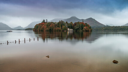 Obraz premium Stunning landscape image of Derwentwater in English Lake District during late Summer with still water and misty mountains in the distance