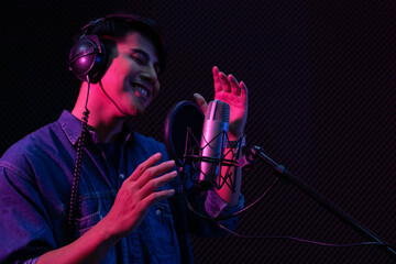 Young Asian man singing to condenser microphone in studio. Professional male vocalist wearing...