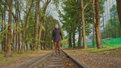 Obraz premium A young guy confidently moves to the camera in the park on the track, a stylishly dressed teenager.