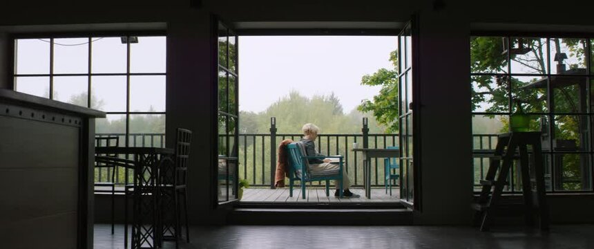 Senior adult mature Caucasian female reading a book on an outdoor terrace of her house on a misty morning. Happy retirement concept. Shot on RED cinema camera with 2x Anamorphic lens