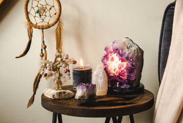 Relaxing home shrine with relaxing objects, amethyst cluster geode lamp illuminated, scented candle burning, selenite tower stone, crystal wire tree and dream catcher.