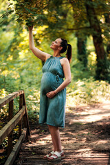 Pregnant woman in a dress walking through the forest.