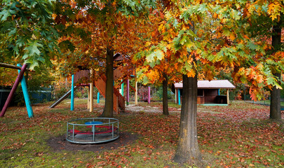 Kinderspielplatz in leuchtenden Farben. Die Laubbäume haben ihre Blätter fallen lassen. Es ist...