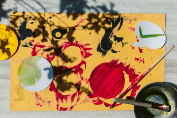 Directly above shot of paint brush and watercolors on yellow card sheet. Creative art work for children, top view