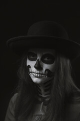 Girl with a skeleton make-up on her face on a dark background with a sad expression