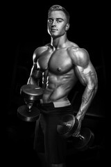 Fototapeta na wymiar Perfect fit athletic guy workout with dumbbells. Handsome power athletic man in training pumping up muscles with dumbbells in a gym. Fitness muscular body isolated on dark background.