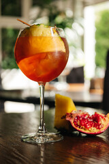 Glass of ice cold Aperol spritz cocktail served in a wine glass with pineapple and garnet, placed...