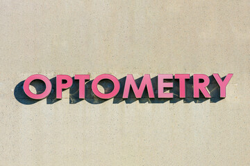 Optometry sign logo in red letters on beige concrete wall