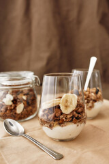 Close up of delicious layered dessert in glass jar, Homemade yogurt with granola and banana, Granola baked with nuts and honey