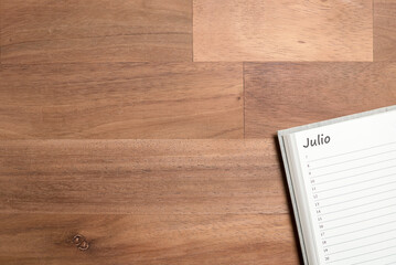 Blank page of a daily planner in Spanish for the month of July, on a wooden desk