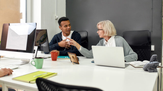 Aged woman, female worker training or teaching new employee, Young man listening to his older colleague while working together in the office