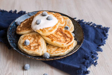 pancakes on a dark blue plate with a blue napkin and frozen blueberries on a light background, soft selective focus