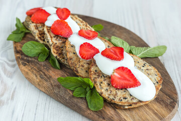 vegetable zucchini pancakes with sesame seeds, served on a wooden board with white yogurt and fresh strawberries, soft selective focus