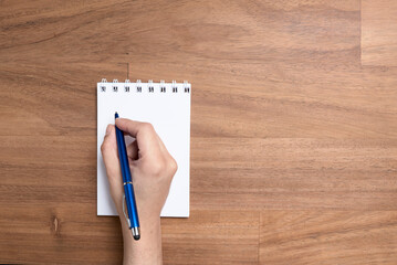 Young hand writing with a blue pen on a blank page of an open notebook