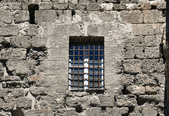 Close-up of the exterior of an old stone house with a window closed with a metal grate, Italy