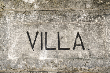 Close-up of a grey, concrete background with the written "villa", Italy