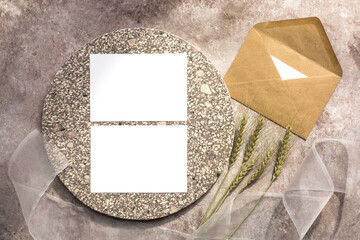 Autumn stationery composition. Blank white memo cards mockup on granite plate, craft envelope, ears of wheat and silk ribbon. Beige grunge background. Top view, flat lay.