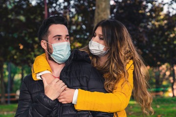 Photo of a young and attractive couple on a date in the park wearing a face mask and hugging